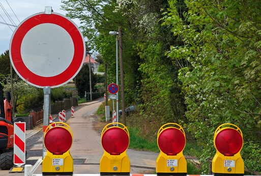 Rot-Weiße Baustellenabsperrung mit vier Warnleuchten | Dahinter eine Straße mit mehreren Warnbarken