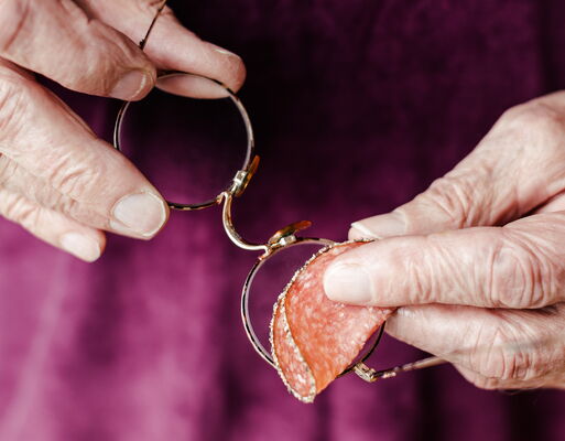 Ein älterer Mensch versucht, seine Brille mit einer Scheibe Salami zu reinigen.