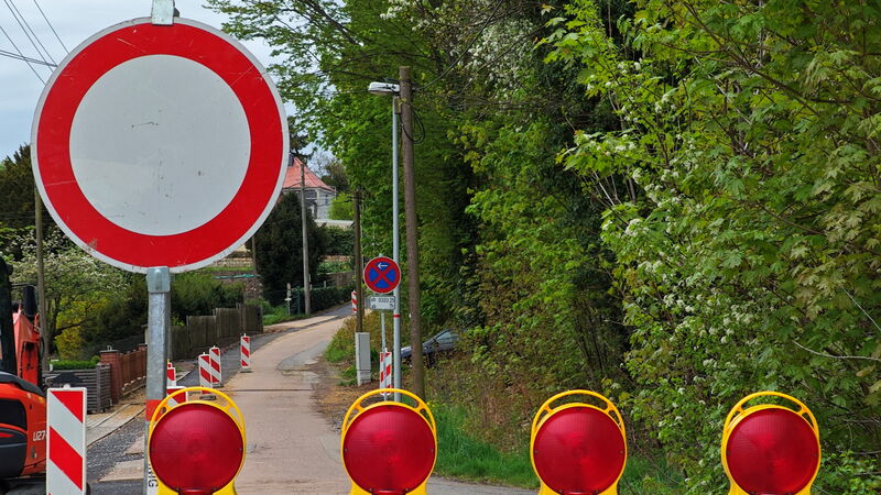 Rot-Weiße Baustellenabsperrung mit vier Warnleuchten | Dahinter eine Straße mit mehreren Warnbarken