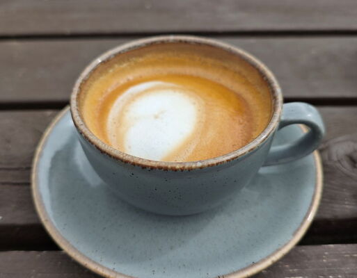 Kaffeetasse aus Keramik mit taubenblauer Glasur, gefüllt mit einem Cappuccino